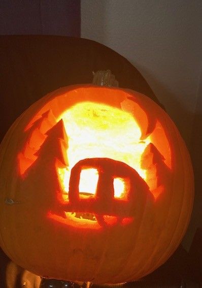 jack-o-lantern carved to a scene with a teardrop trailer and an evergreen tree with a crescent moon above